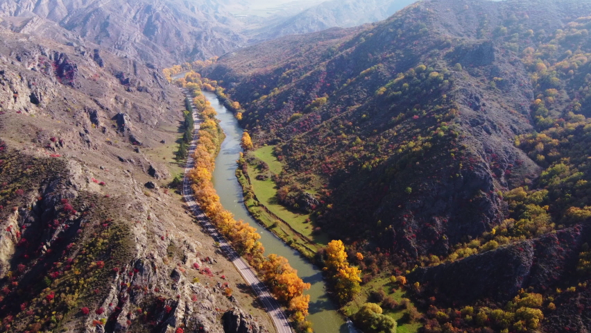 Mountain ridges and lush deciduous trees located on shores of calm river on sunny autumn day in highlands