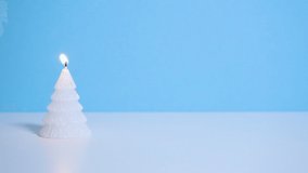 White Christmas tree wax candle burning on blue background. Slow motion full HD video. New Year or Christmas video banner with copy space.