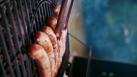 Meat sausages are fried on the grill of the street grill. Cook turns bratwurst over with tongs. Vertical video