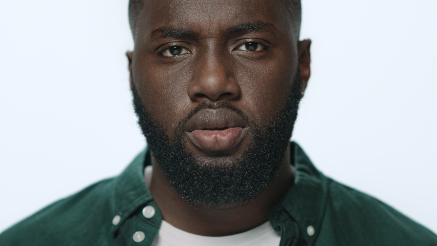 Portrait thoughtful guy looking camera in studio. Closeup pensive male student posing indoors. African american model standing serious face expression at light background. Serious man face expression