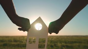 The family's hands are holding a paper house at sunset, the sun is shining through the window. The symbol of the house, happiness. The concept of building a house for the family. Dream to buy a house - Powered by Shutterstock - Get 15% off with code: PIKWIZARD15