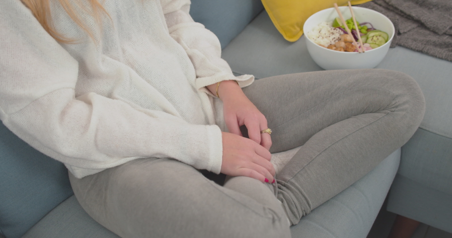 Blond woman eating dinner or meal alone at the sofa inside a room of her house