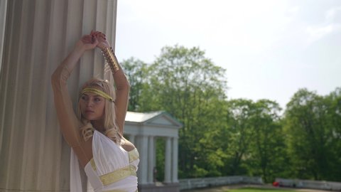 portrait of a blonde in a white toga at the column. the camera is moving