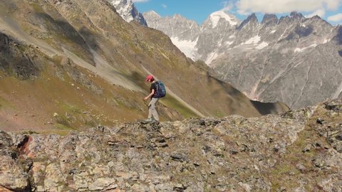 Mountaineering young woman with backpack hiking on rocky mountain ridge in high Caucasus mountains, Georgia. Aerial drone footage of the female tourist walk a trekking trail surrounded by snowy peaks