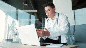 asian doctor advises patient online via video call using laptop and webcam. Remote consultation with a physician. man talking chat with colleagues Telemedicine, telehealth. modern surgery office