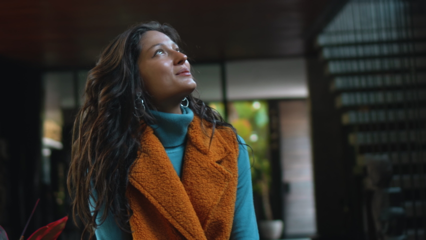 Young and beautiful European girl long-haired brunette sits at home on a table in autumn clothes and a yellow sweater and smiling looks forward swaying her feet