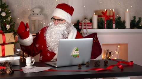 Santa Claus preparing Christmas gifts. He counts boxes and types on a laptop.