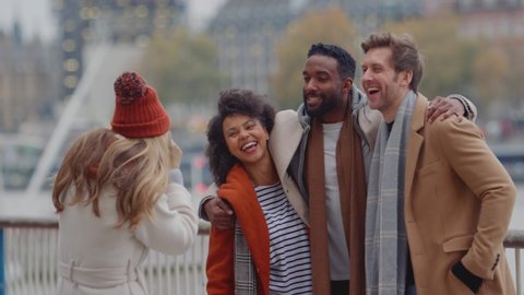 Group of friends outdoors wearing coats and scarves posing for photos on camera on autumn or winter trip to London - shot in slow motion Video stock