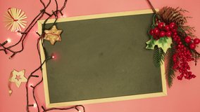 A man's hand writes with chalk Merry Christmas on a black board. There is an asterisk, a coniferous branch and colored lights. Dad makes a Happy New Year greeting manuscript. Flat laid holiday items.
