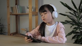 Cute little kid girl in headphones using digital computer tablet, enjoying cool video or photo content in social network, reading, playing online games, listening the music. Technology addicted. 