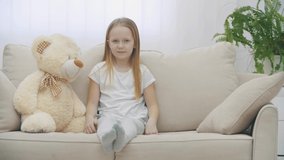4k slowmotion video of little girl sharing secrets with teddy bear on the sofa.