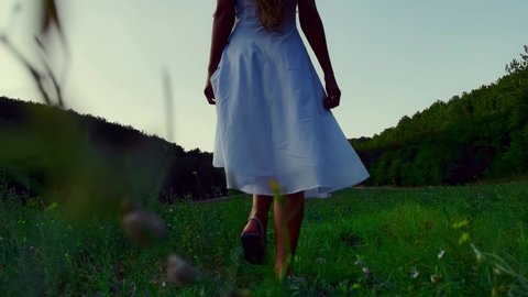 A beautiful, slender, young girl in a white dress with long hair runs along a green field! Hair fluttering in the wind. The dress flutters. A young, virgin girl runs gracefully. A beautiful cinematic 