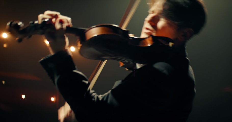 CU HANDHELD Portrait of young aspiring musician playing violin on a stage of a large venue. Shot with 2x anamorphic lens Royalty-Free Stock Footage #1083442696
