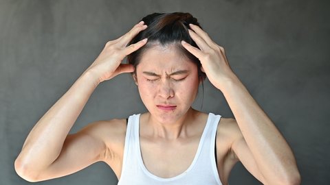 Asian woman having headache and she trying to do head massage by herself. Massage helps ease muscle spasms and knots in parts of the body prone to tightness and tension.