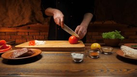 The cook cutting red tomatoes on a wooden board with a knife. 