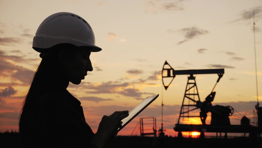 Industrial, oil and gas concept. Silhouette working engineer oil rig. Oil rigs at sunset. Silhouette of woman engineer with tablet overseeing the site of crude oil production at sunset.