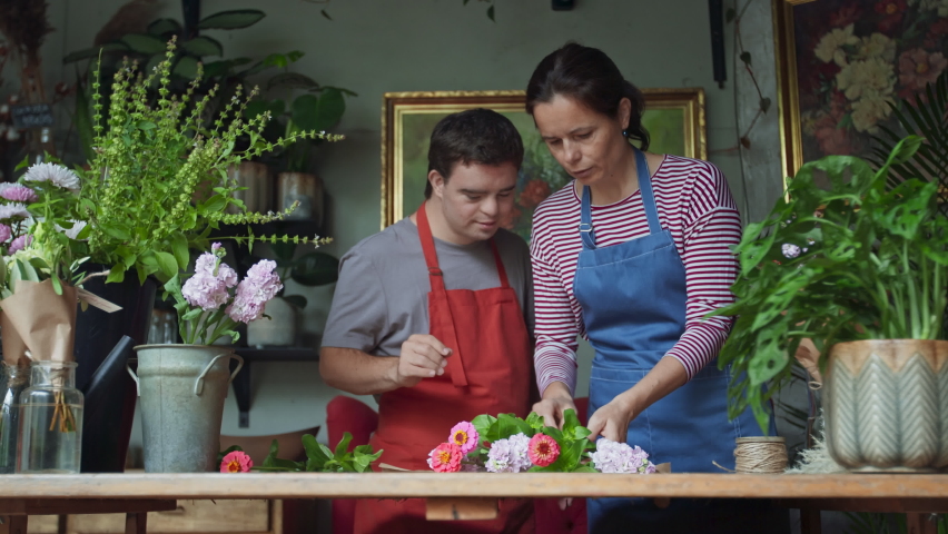 Young male florist with Down syndrome working with help of mentoring colleague indoors in flower shop | Shutterstock HD Video #1083453361