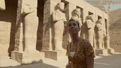 Young woman sightseeing ancient Egyptian temple in Luxor. Tracking shot: Woman walking pass Pharaoh status on vacation 