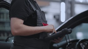 A mechanic in a close-up car service holds a tablet in his hands and presses the screen near the car - Powered by Shutterstock - Get 15% off with code: PIKWIZARD15