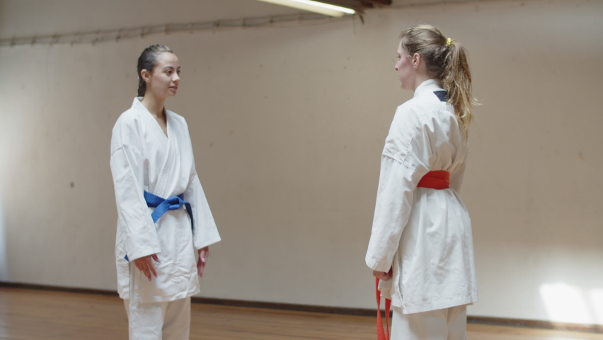 Long shot of focused girls practicing karate movements in gym. Concentrated martial artsists in white kimonos having karate class, exercising, preparing for competition. Sport, training concept