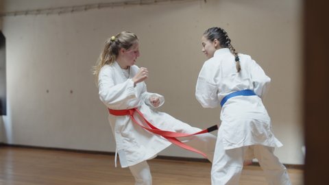 Long shot of focused girls practicing karate movements in gym. Concentrated martial artsists in white kimonos having karate class, exercising, preparing for competition. Sport, training concept