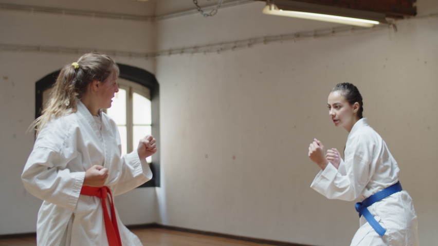 Tracking shot of focused girls having karate class in gym. Medium shot of concentrated teenagers training together, doing physical activity, devoting time to hobby. Martial arts, sport concept
