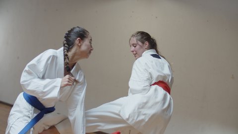 360 degree shooting of girls practicing karate in gym. Focused and excited Caucasian martial artsists in kimonos training in practice room, having karate class. Sport, training concept