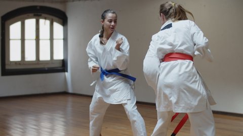 Tracking shot of serious girls in kimonos fighting in gym. Medium shot of focused teenagers practicing karate, improving professional skills while training together. Sport, martial arts concept