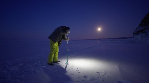 Man drill hole with hand auger at frozen ice. Shadow spin around in head light