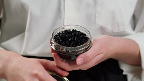 Black caviar close-up. Chef opening glass bow with beluga sturgeon roe. Raw seafood. Luxury delicacy food. Delicious and tasty fish products. Russian cuisine. Festive dinner.