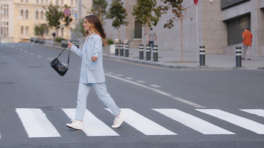 Young beautiful girl model business woman student in stylish blue suit with black handbag walking jumping circling rotation on crosswalk in city on road pedestrian crossing happiness fun walk dancing Royalty-Free Stock Footage #1083463702