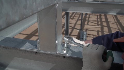 A builder wearing a helmet and gloves tightens a bolt with a metal wrench. close-up back view. Bolted. Cutting metal using modern processing technologies. works at a height