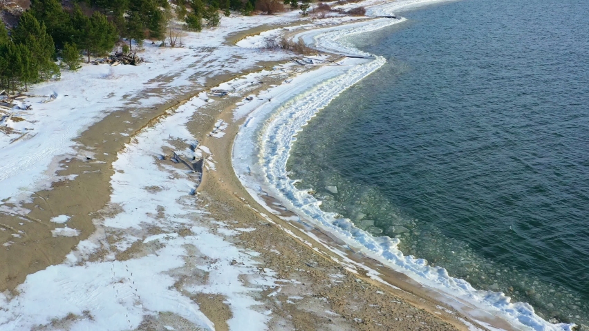 The surface of the freezing sea near the sandy shore. Ice floes float along the shore. There is snow on the shore. Drone view.