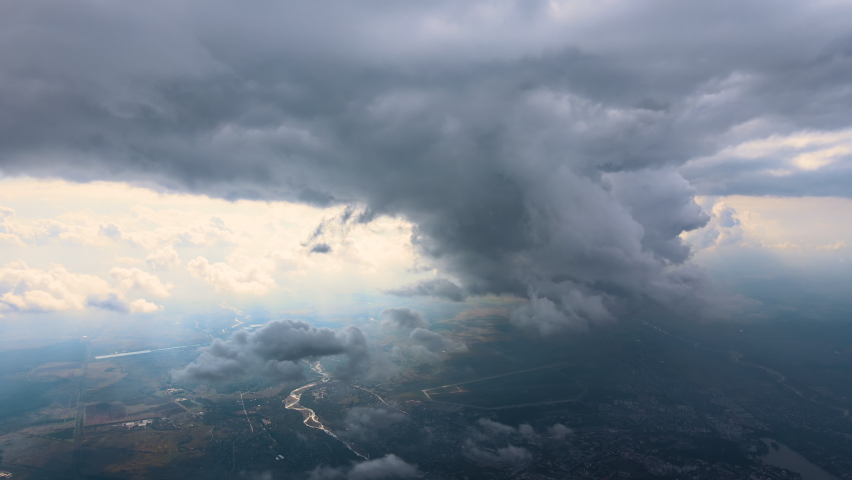 Aerial view from airplane window at high altitude of distant city covered with puffy cumulus clouds forming before rainstorm