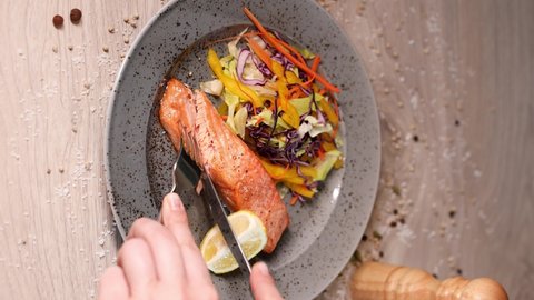 Salmon with fresh vegetables, cuts with a fork and knife. Vertical Screen 4K