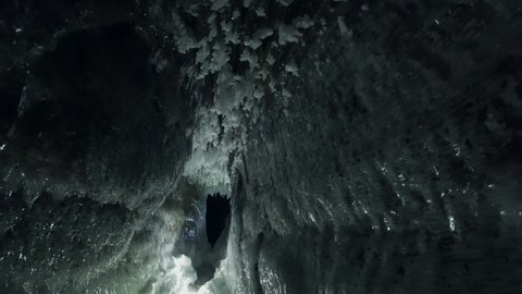 Walk forward inside dark night winter frozen cave grotto. Mystical ice floes of sharp icicles on walls. Baikal lake nature landmark movie. Dangerous claustrophobia Fairytale dungeon. Russia Siberia