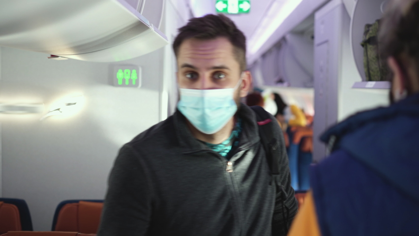 Male passenger in covid-19 face mask and backpack walking past other people to take his seat. Traveling, tourism during coronavirus pandemics. Travelers with maksed faces on plane board during flight Royalty-Free Stock Footage #1083485269