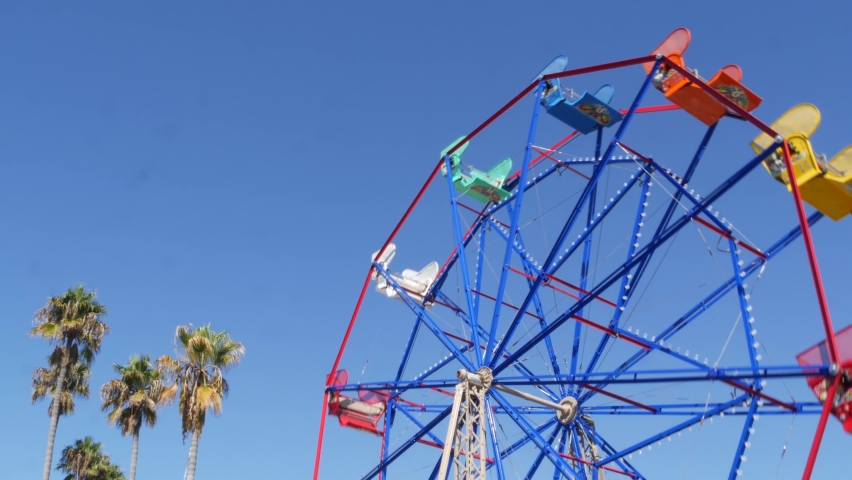 Classic vivid summertime, fun and childhood symbol, green tropical palm tree leaves. Iconic colorful retro ferris wheel attraction. Newport, california pacific ocean beach resort near Los Angeles USA.