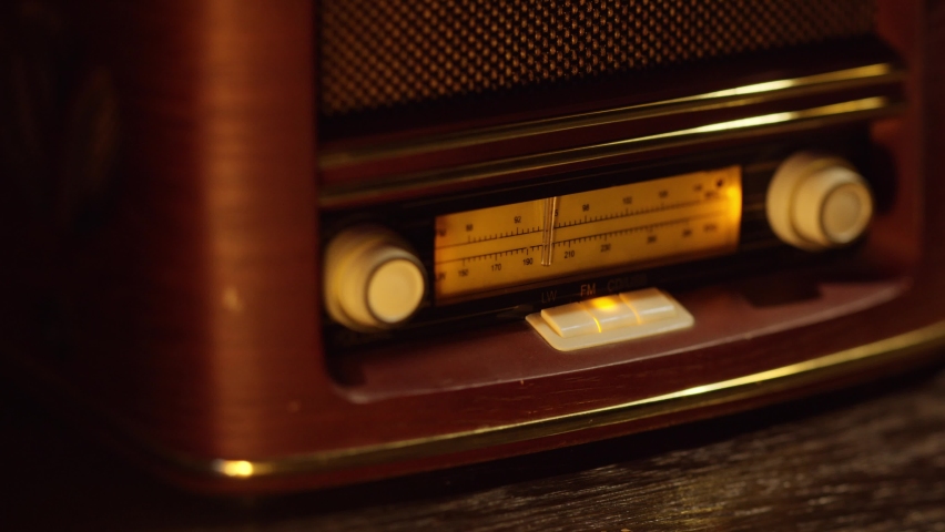 Vintage wooden retro radio receiver, macro shot of manual tuning of radio waves, hand turns the tuning knob. Slow camera movement from left to right. Royalty-Free Stock Footage #1083489628