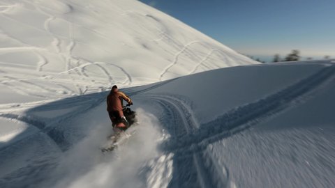 Aerial view man extreme riding on snowmobile surrounded by snowy slope Mamdziskha mountain sports FPV drone. Enjoying speed driving at wilderness nature landscape Black Sea Abkhazia sunny day