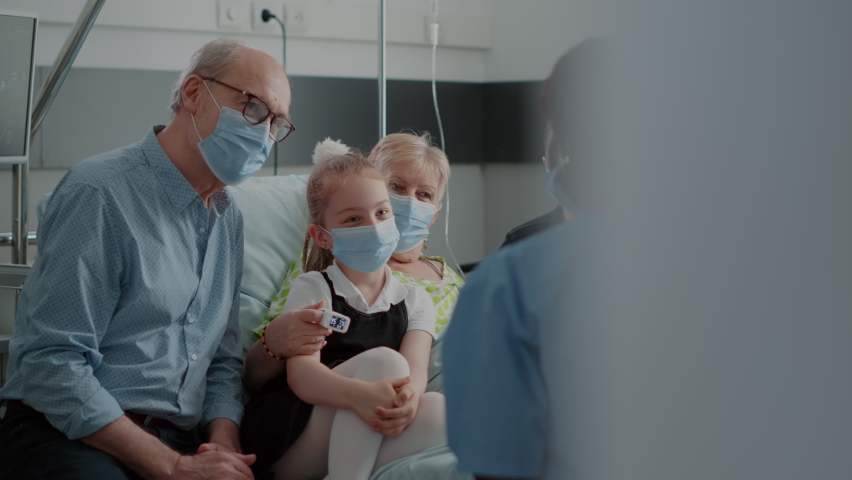 Nurse giving recovery advice to patient and visitors with face mask in hospital ward. Medical assistant helping with medication at checkup visit, talking to sick woman and family during pandemic. | Shutterstock HD Video #1083493633