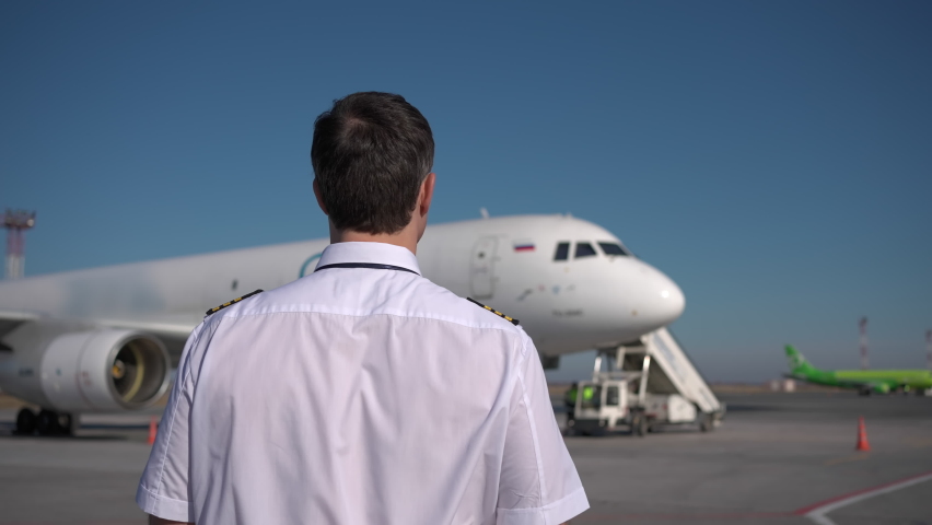 Airport, pilot, airplane. Follow footage of confident male pilot in uniform walking on runway in background plane, aircraft, Travel professional captain travelling transportation professions people