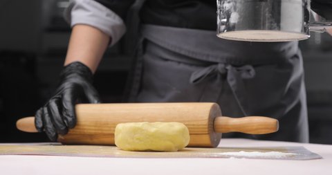 The baker or chef is about to roll the dough on a white table, dusting it with flour so that it doesn't stick to the rolling pin as it rolls out. Close-up of hands in black gloves. Baking concept.