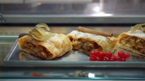 Apple strudel. sweet pastries are sold in the cafe. apple pie baked desserts with fruits inside and with red berries, physalis and cinnamon on top on a glass showcase, close-up, dolly shot.