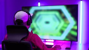 Rear view young Player video computer pc hands on head feeling stressed. Young man sitting on chair in game station.Streamer wearing headphone playing action game online and lose