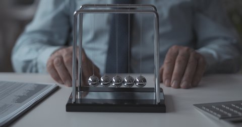 Corporate businessman sitting at desk and playing with Newton's cradle balance balls