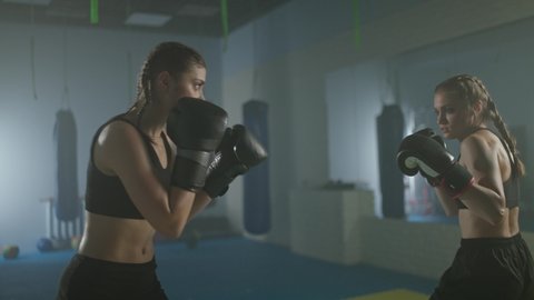 Training battle of two female fighters, training in the boxing gym, females train defence and series of punches.