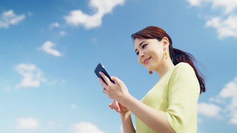 Young asian woman using a smartphone under the blue sky.
