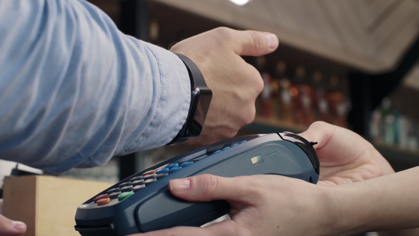 Pay by smart watch on pos terminal at coffee bar. E-money transfer from electronic wallet. Payment machine or card reader in barista hand closeup. Smartwatch of male buyer in food market or restaurant | Shutterstock HD Video #1083505699