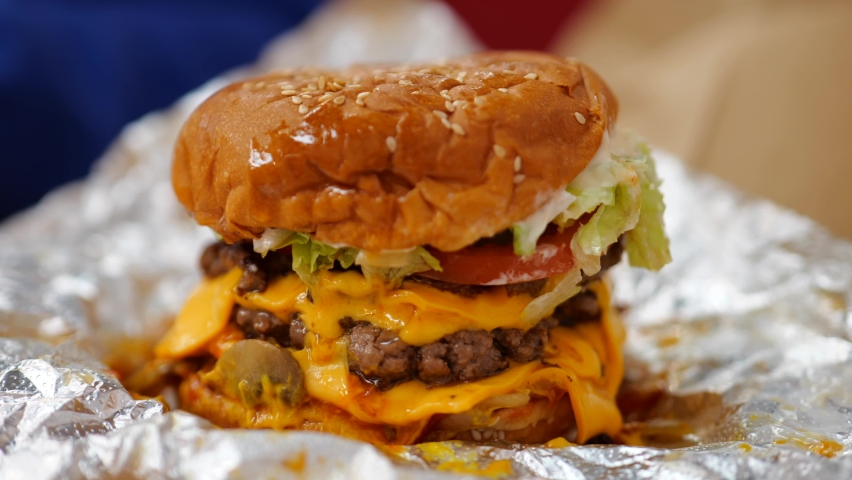 A piece of lettuce falls from the side of an enormous cheeseburger